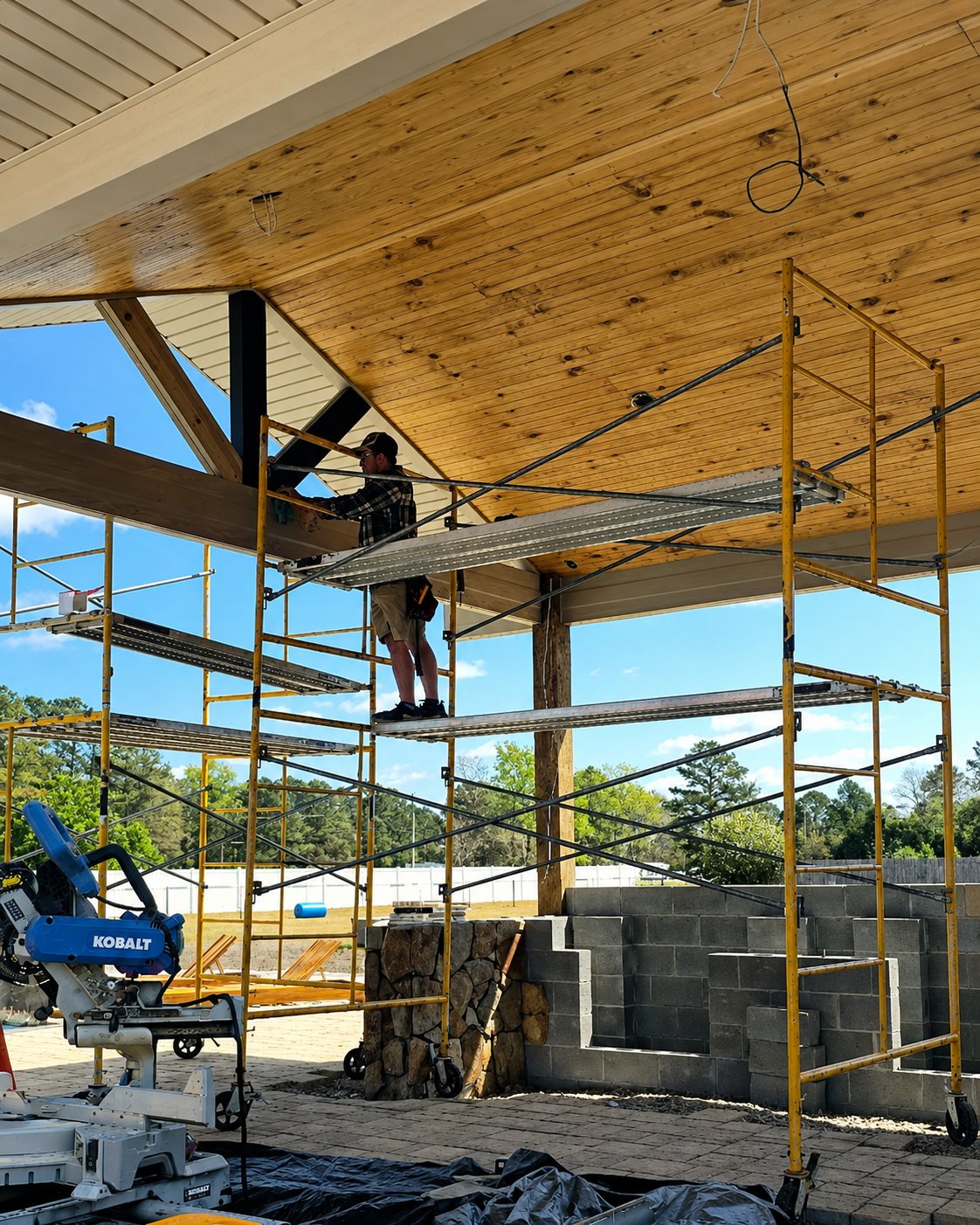 Carpenter installing a pine tongue-and-groove pavilion ceiling from scaffolding on a Craven County, NC outdoor living build